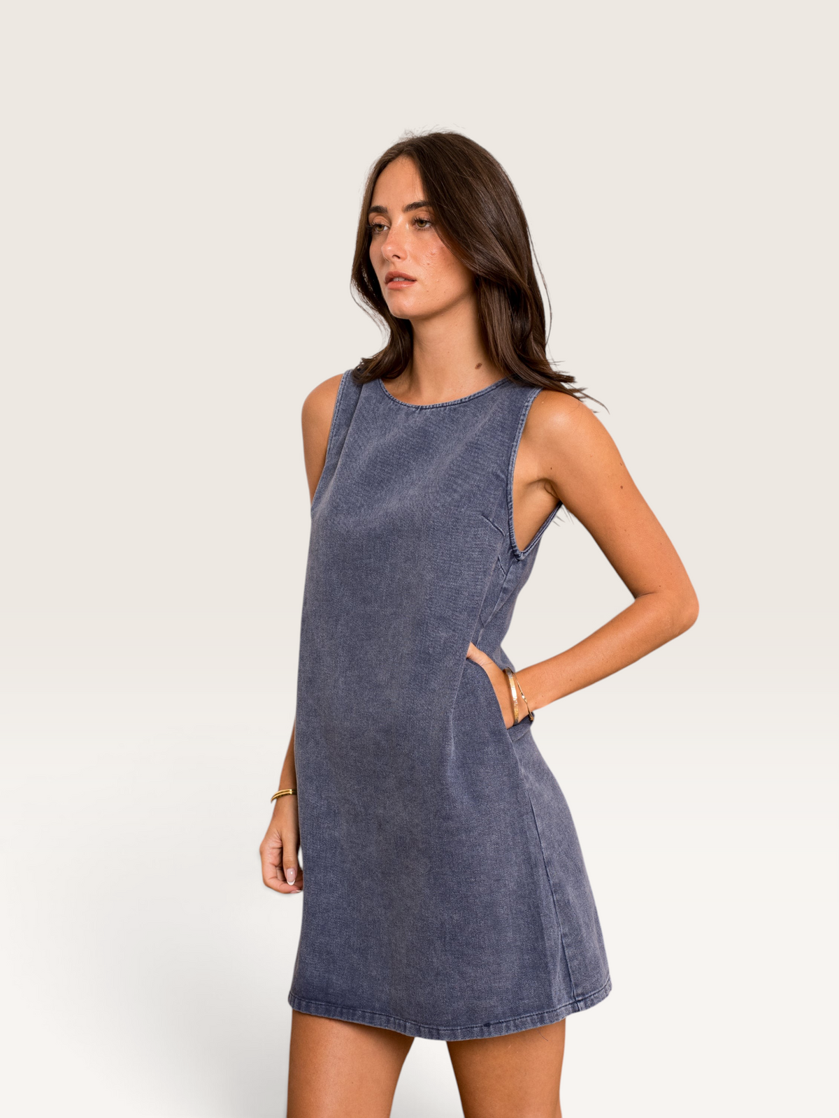 Robe courte en jean bleu Sable_blanc_collection sans manches avec poches latérales portée par une femme